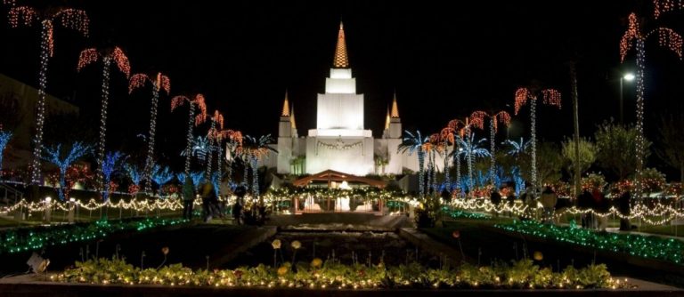 The Oakland Temple at Christmas. Several Christmas lights can be seen throughout the image in shrubbery and around the trunks of palm trees.