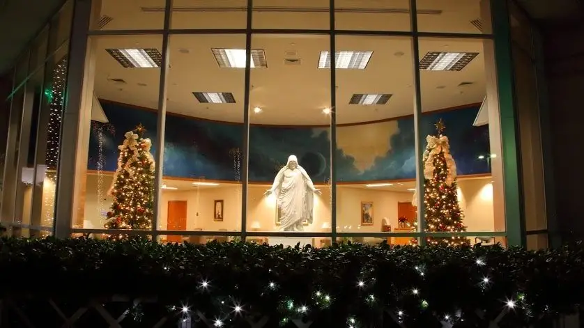 The Christus in the Oakland Temple Visitors' Center at Christmas. Several Christmas lights can be seen, as well as Christmas trees.