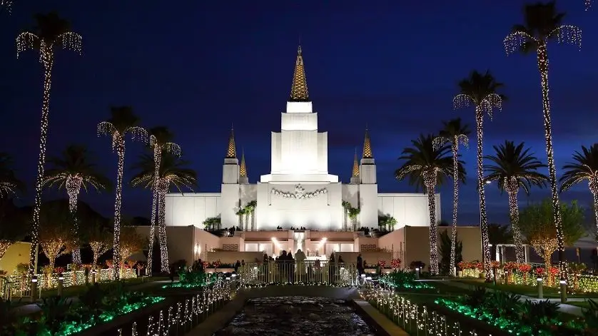 The Oakland Temple at Christmas. Palm trees, plants, and the grounds are covered in Christmas lights.