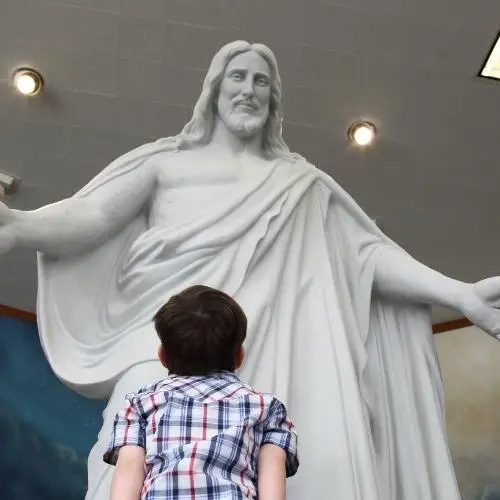 A young boy looking looking up at the Christus statue in the Oakland California Temple Visitors' Center at Temple Hill.